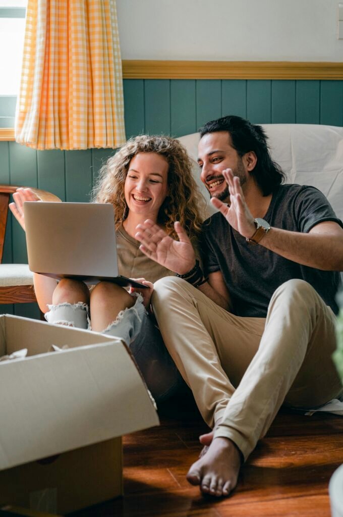 A happy couple in Ontario, possibly after a move, is video chatting on a laptop with open moving boxes around them.