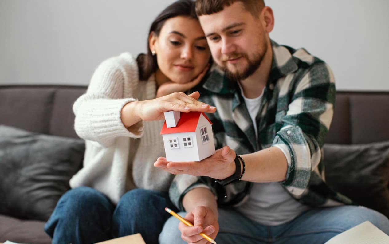 A couple in Ontario is looking at a small model house, potentially symbolizing their first home purchase.