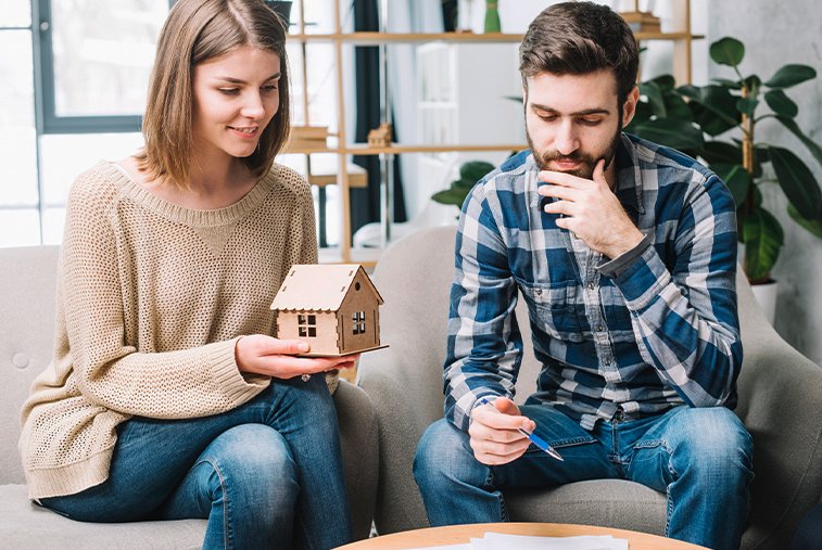 Couple discussing home equity loan options while holding a wooden house model, symbolizing property investment planning