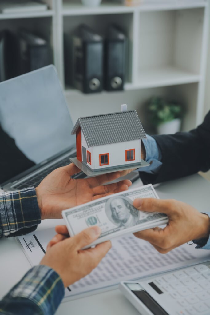 In Ontario, hands exchange a model house for a stack of US dollar bills over paperwork and a laptop, possibly illustrating a quick mortgage approval process.