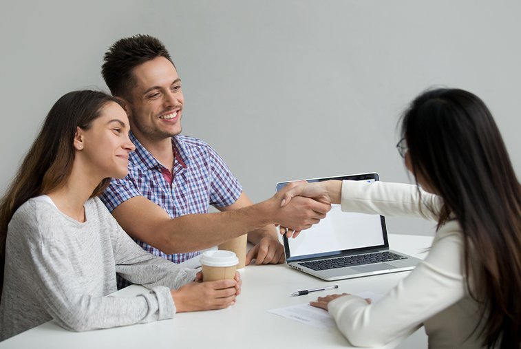 A smiling couple in Ontario shakes hands with a woman, possibly a mortgage agent, signifying their mortgage pre-approval.