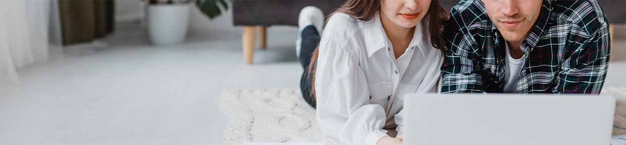 Couple lying on the floor and looking at a laptop together, researching home financing or second mortgage options.
