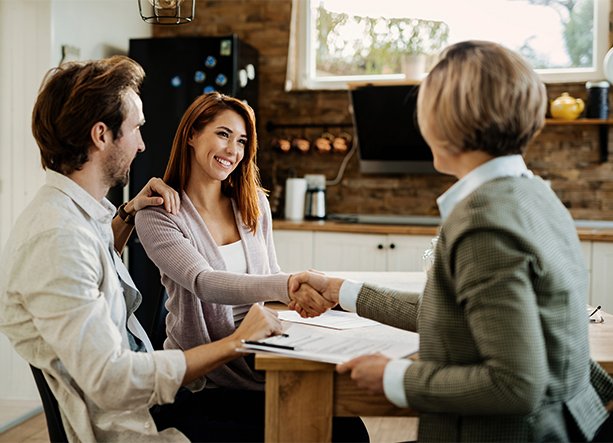 Smiling couple meeting with a financial advisor, shaking hands over paperwork at a kitchen table, symbolizing agreement on a second mortgage.