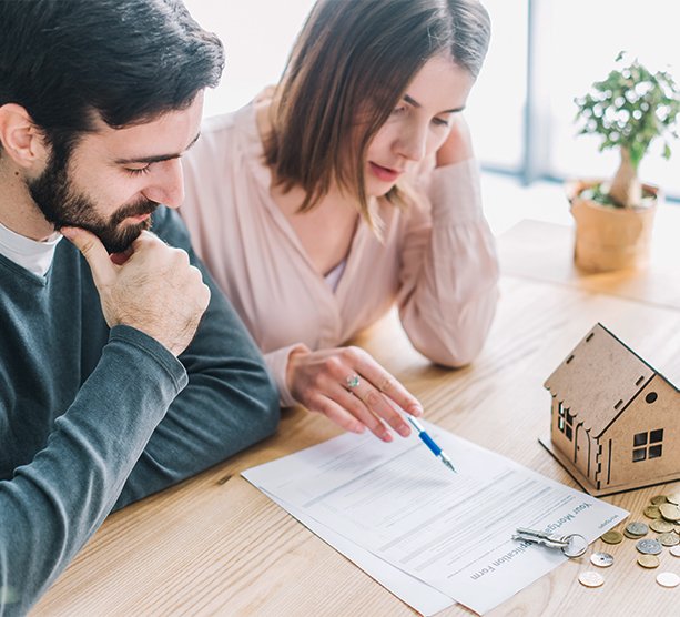 Couple reviewing mortgage documents at a table with a small house model and keys, considering the benefits of a second mortgage.
