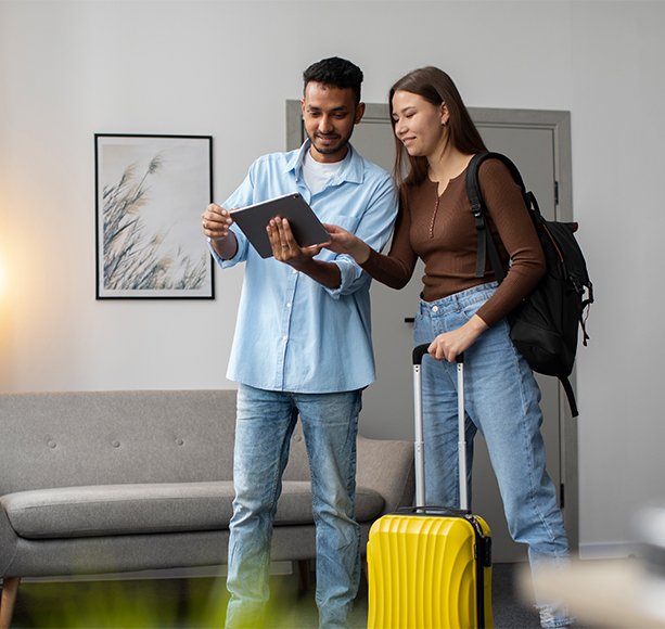 Young couple with luggage reviewing travel plans on tablet, representing vacation or second home possibilities.