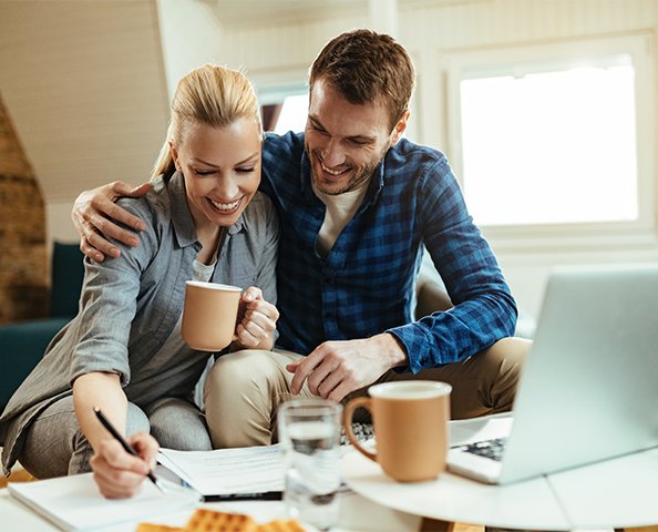 Happy couple planning finances at home with laptop and coffee, possibly discussing a second home mortgage.